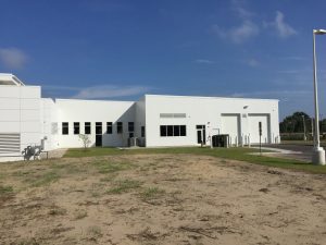 Large industrial building with smooth sheet metal paneling, driveway leading to overhead garage door